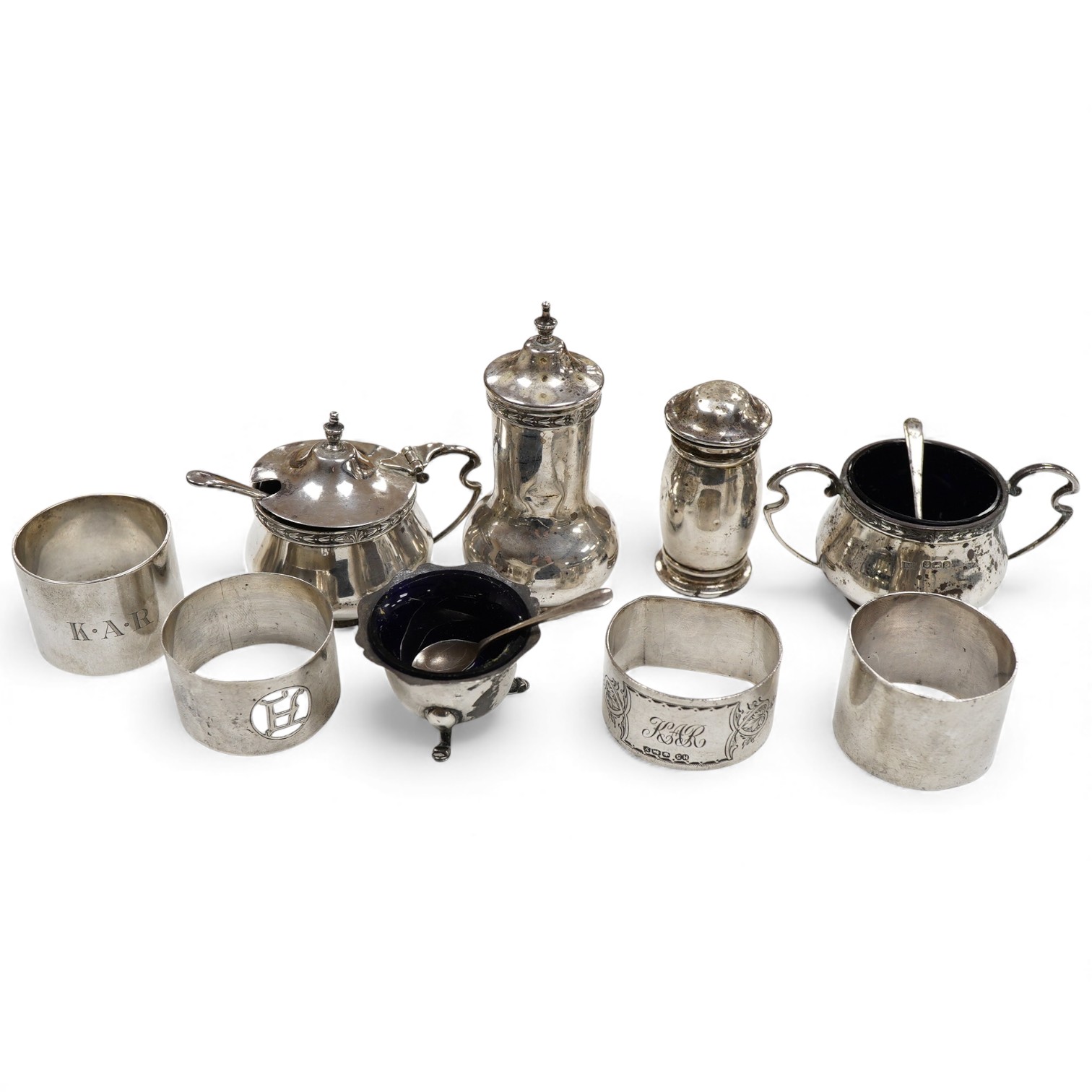 A George V silver three piece condiment set by Walker & Hall, Sheffield, 1921, together withy two other silver condiments, three assorted silver condiment spoons and four assorted silver napkin rings.